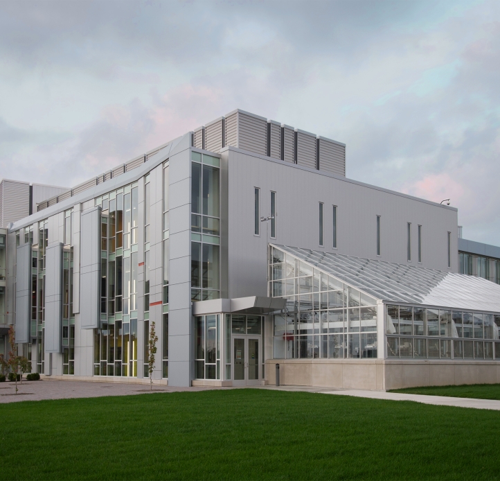 Science & Mathematics Complex - A modern, multi-story science building featuring large glass windows, a light-colored facade, and an attached greenhouse sits on a manicured lawn under a cloudy sky.